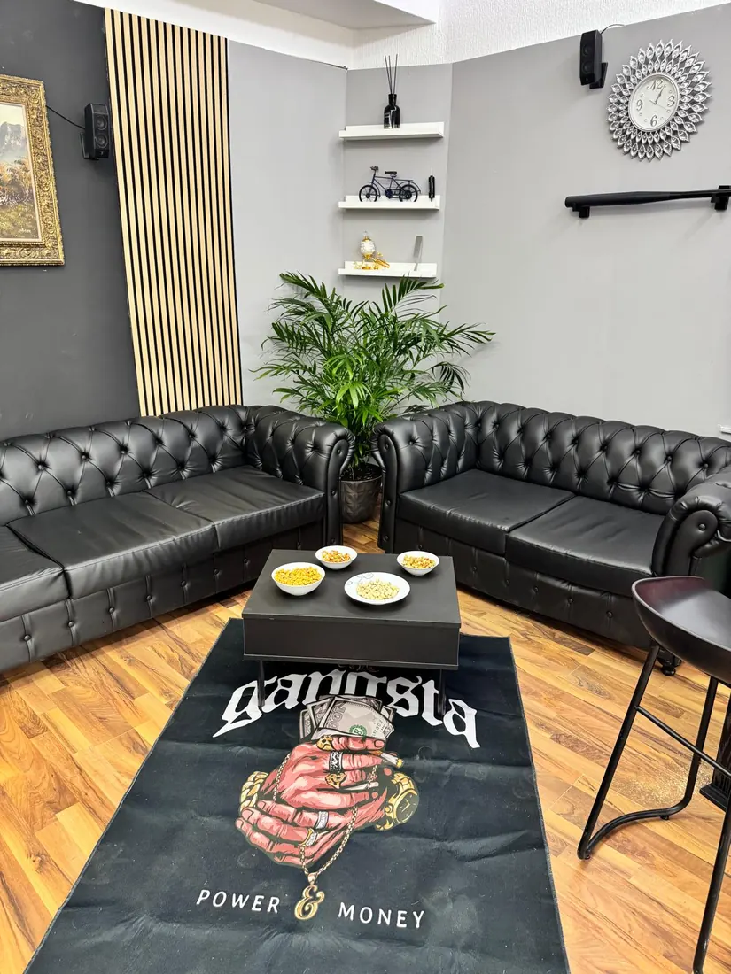 Lounge-Bereich im Babo Barbershop Köln-Mülheim mit schwarzen Chesterfield-Sofas und warmem Holzboden